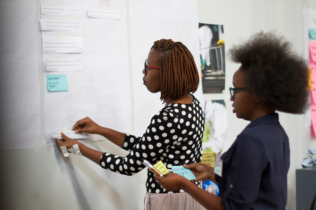 two ugandan women looking at white wall with post its